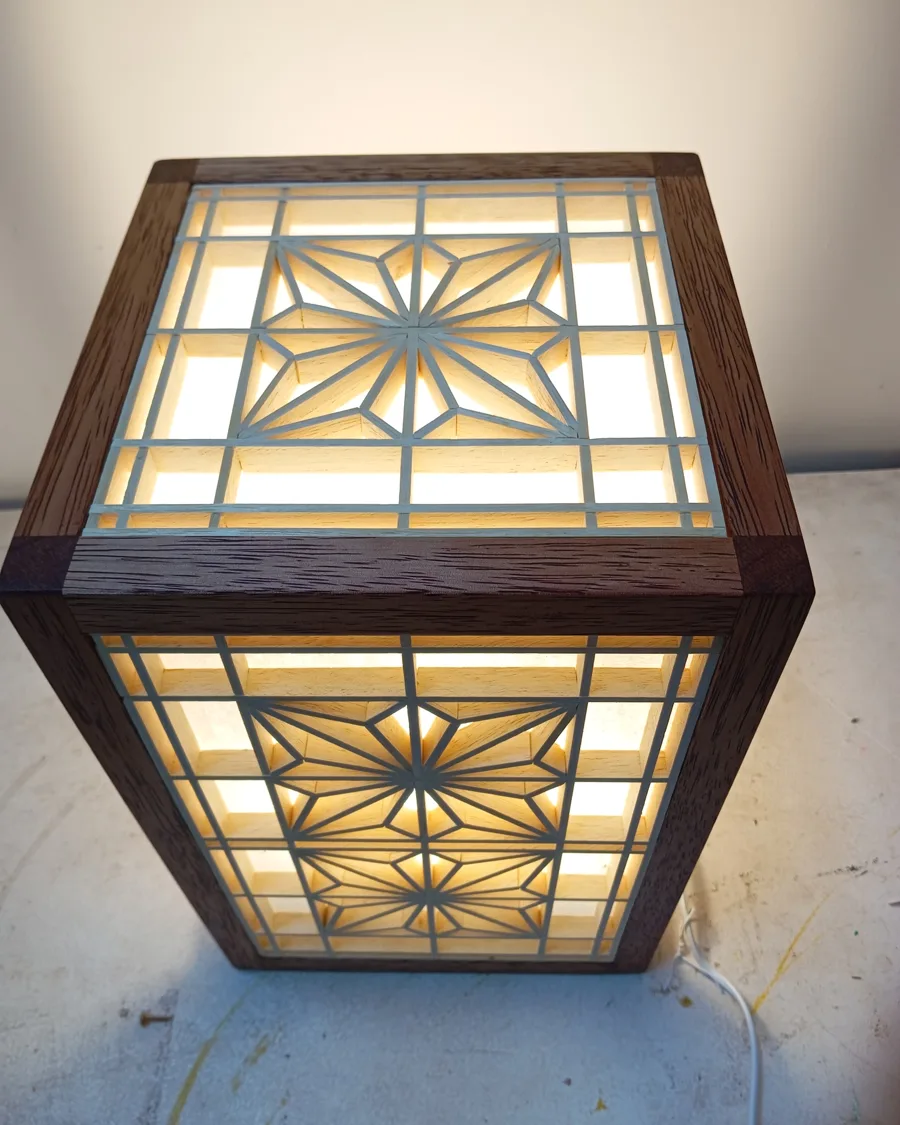 Lámpara de madera encendida, con paneles kumiko de patrón asanoha que tamizan la luz.